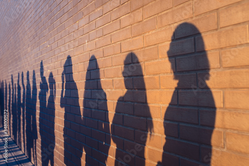 People crowd shadows lined up against a red brick wall. They are in a queue for changes in life. Social distance, covid and immigration issue concept photo