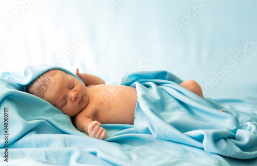 Obraz na płótnie Little newborn baby resting on soft, delicate fabric of blue blanket. Baby falling asleep covered with blanket. w salonie