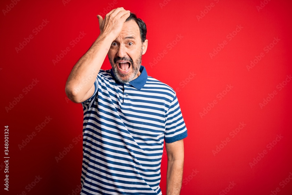 Middle age hoary man wearing casual striped polo standing over isolated red background surprised with hand on head for mistake, remember error. Forgot, bad memory concept. Middle age hoary man wearing casual striped polo standing over isolated red background surprised with hand on head for mistake, remember error. Forgot, bad memory concept.