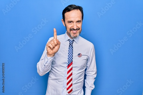 Middle age handsome patriotic businessman wearing united states tie over blue background smiling with an idea or question pointing finger up with happy face, number one