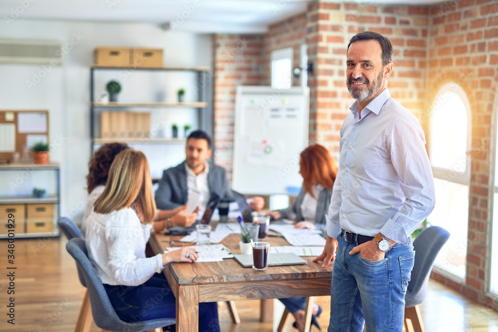 Group of business workers working together. Middle age handsome businessman standing smiling happy looking at the camera at the office Group of business workers working together. Middle age handsome businessman standing smiling happy looking at the camera at the office