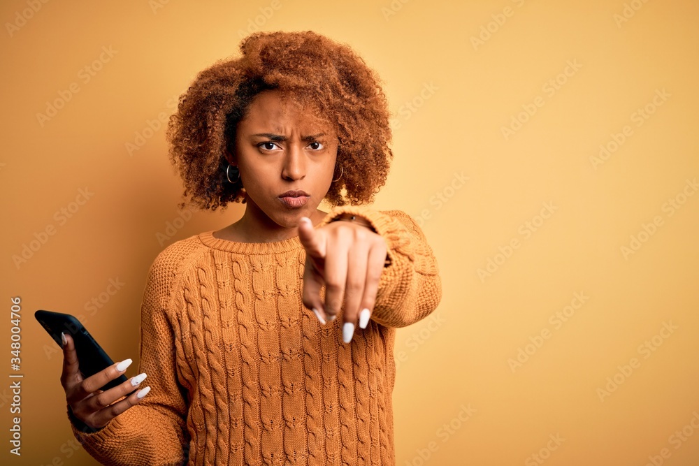 Young African American afro woman with curly hair having conversation using smartphone pointing with finger to the camera and to you, hand sign, positive and confident gesture from the front Young African American afro woman with curly hair having conversation using smartphone pointing with finger to the camera and to you, hand sign, positive and confident gesture from the front