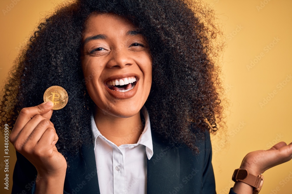 Young african american business woman with afro hair holding bitcoin over yellow background very happy and excited, winner expression celebrating victory screaming with big smile and raised hands Young african american business woman with afro hair holding bitcoin over yellow background very happy and excited, winner expression celebrating victory screaming with big smile and raised hands