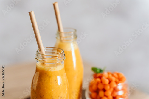 Bright sea buckthorn smoothie on a rustic board. berries, ginger, glass bottles, paper tubes. no plastic. healthy food