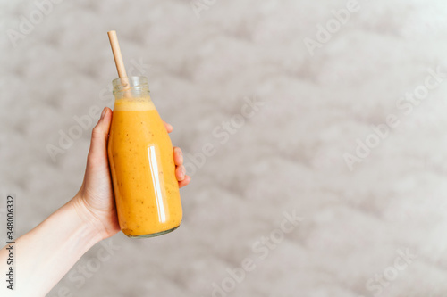 hand holds glass transparent bottle with orange smoothie. sea ​​buckthorn smoothie. The concept of a healthy food, diet, detox.