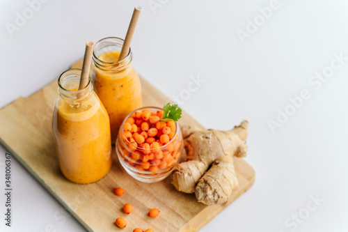 Bright sea buckthorn smoothie on a rustic board. berries, ginger, glass bottles, paper tubes. no plastic. healthy food