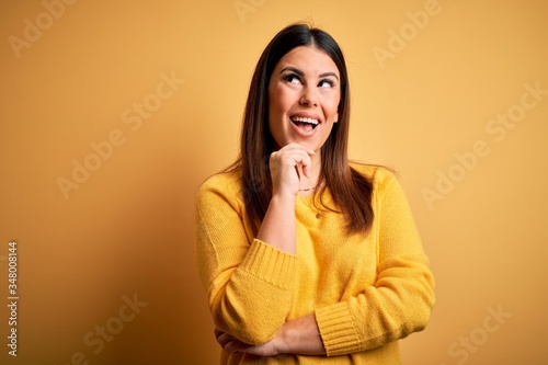 Young beautiful woman wearing casual sweater over yellow isolated background looking confident at the camera with smile with crossed arms and hand raised on chin. Thinking positive.