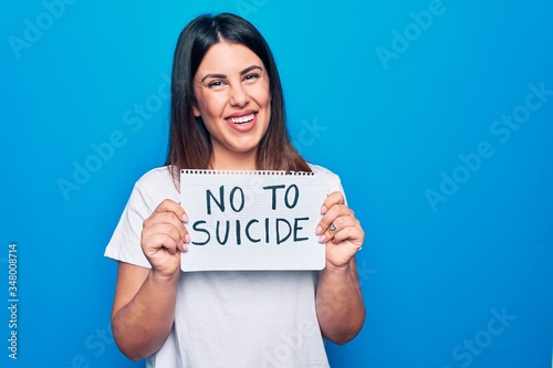 Young beautiful woman asking for psychical problem holding paper with not to suicide message looking positive and happy standing and smiling with a confident smile showing teeth