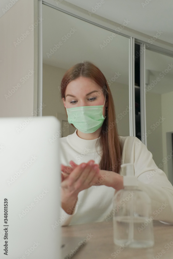 A beautiful girl works from home in a medical mask and rubs an antiseptic in her hands. A beautiful girl works from home in a medical mask and rubs an antiseptic in her hands.