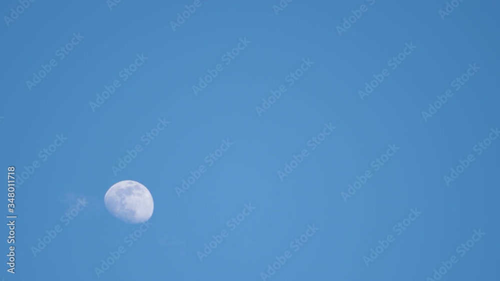 Waxing gibbous moon rising with a clear blue sky, light clouds roll through frame Waxing gibbous moon rising with a clear blue sky, light clouds roll through frame