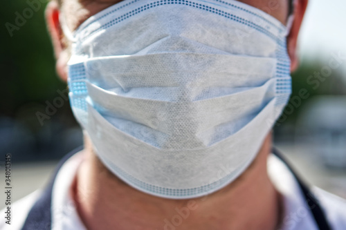 A man in a protective medical mask stands on a city street. Virus protection. Pandemic, epidemic and medicine. Shallow depth of field photo