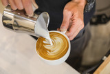 Close up of barista hand pouring stremed milk into white cup of hot coffee to create latte art.
