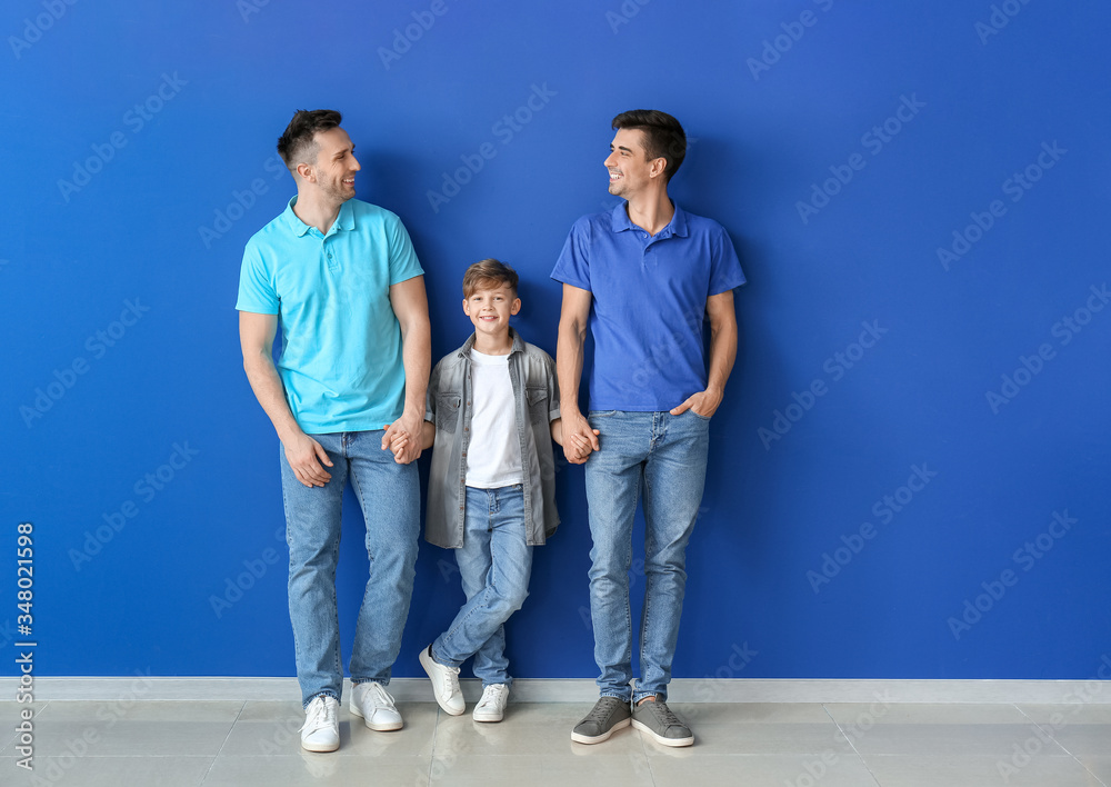 Happy gay couple with adopted child near color wall