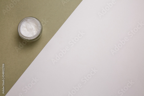 Open jar of cream on the background of white and khaki.