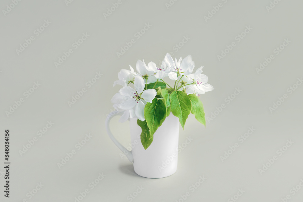 white style elongated porcelain mug full of white blooming flowers with green fresh leaves. The cup is used as a vase. Idea for Cozy Home Decor