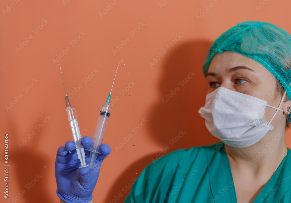 A doctor wearing a protective mask and gloves shows a syringe with a vaccine to work with the covid-19 coronavirus pandemic during the epidemic A doctor wearing a protective mask and gloves shows a syringe with a vaccine to work with the covid-19 coronavirus pandemic during the epidemic