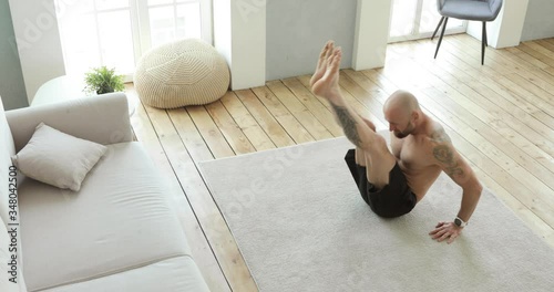 Muscular man is doing abs exercises crunches on floor at home pulls his legs to chest sitting on floor. Sport and fitness. Training, workout and wellness concept. High-intensity interval training. photo