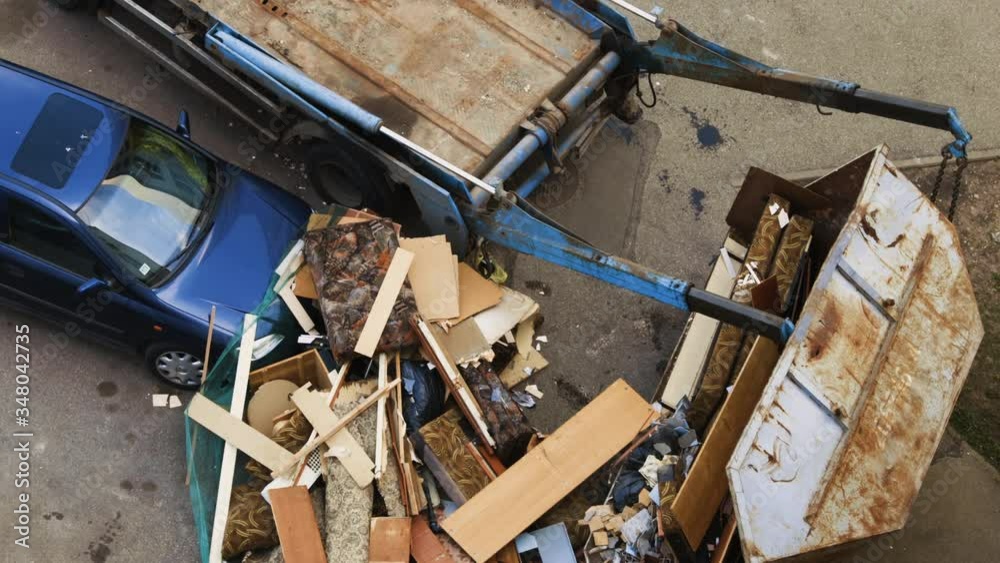 Truck moves fallen garbage container. Trash damaged blue car Truck moves fallen garbage container. Trash damaged blue car