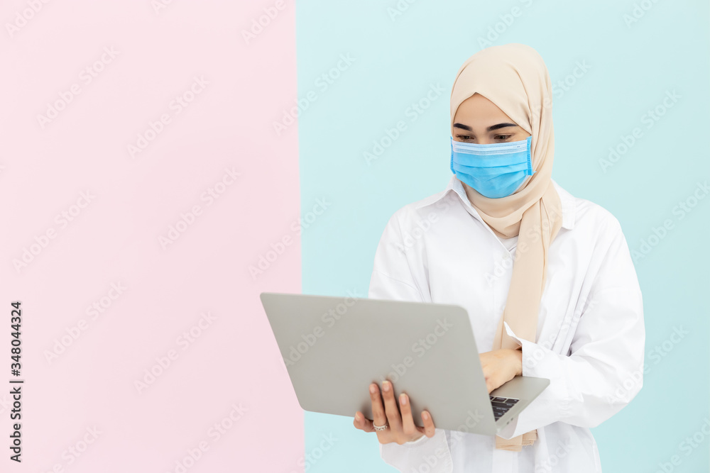 asian muslim woman wearing medical face mask for prevent infection virus with laptop on pastel background, Coronavirus(covid-19) concept. asian muslim woman wearing medical face mask for prevent infection virus with laptop on pastel background, Coronavirus(covid-19) concept.