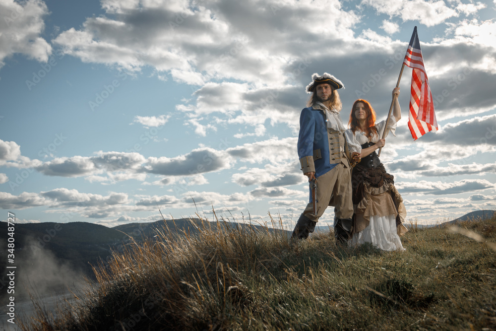 Man in form of officer of War of Independence and girl in historical dress of 18th century. July 4 is US Independence Day. Couple of patriots freedom fighters in outdoor on background cloudy sky