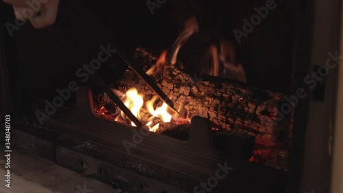 Young man moving the burning logs around inside fireplace with metal pliers, still medium close up shot photo