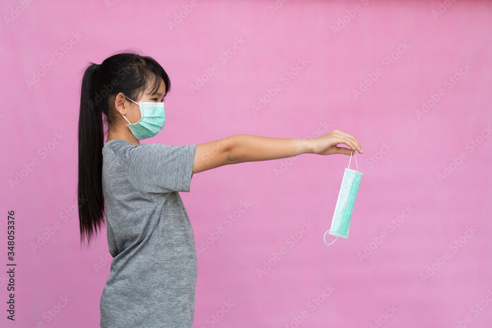 Little girl has sterile medical  mask protect herself from Coronavirus COVID-19 isolated on pink background, child with a mask on her nose for safety outdoor activity, illness or air pollution