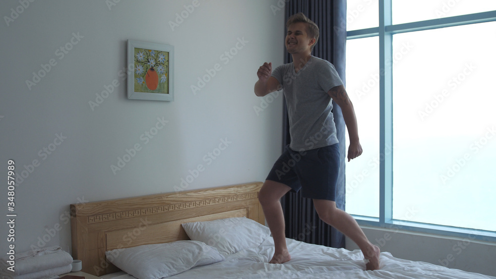 Handsome man have fun, jumping, dancing on bed by the window Handsome man have fun, jumping, dancing on bed by the window