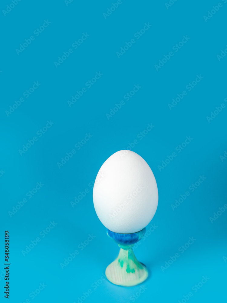 a whole unpainted white egg on a stand on a blue background in the center of the frame a whole unpainted white egg on a stand on a blue background in the center of the frame