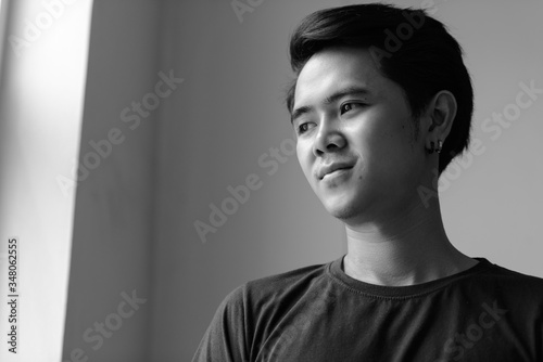 Portrait of young Asian man by the window indoors in black and white