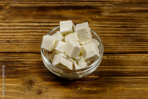 Feta cheese cubes in glass bowl on a wooden table
