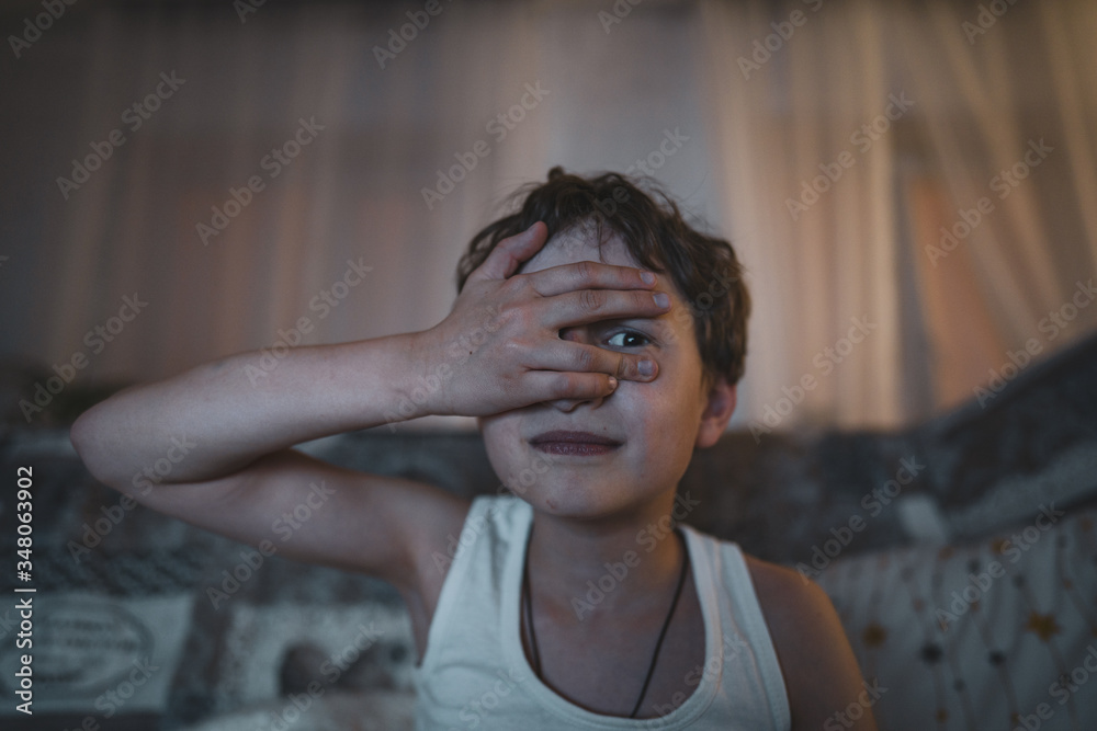 Small emotional boy covers his face with his hand, watching a horror movie Small emotional boy covers his face with his hand, watching a horror movie