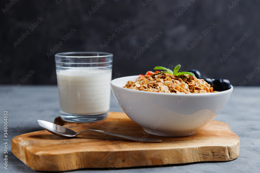 A plate with granola or oatmeal muesli is on a wooden stand next to a glass of milk. Save the space. Healthy, diet breakfast at home. A plate with granola or oatmeal muesli is on a wooden stand next to a glass of milk. Save the space. Healthy, diet breakfast at home.