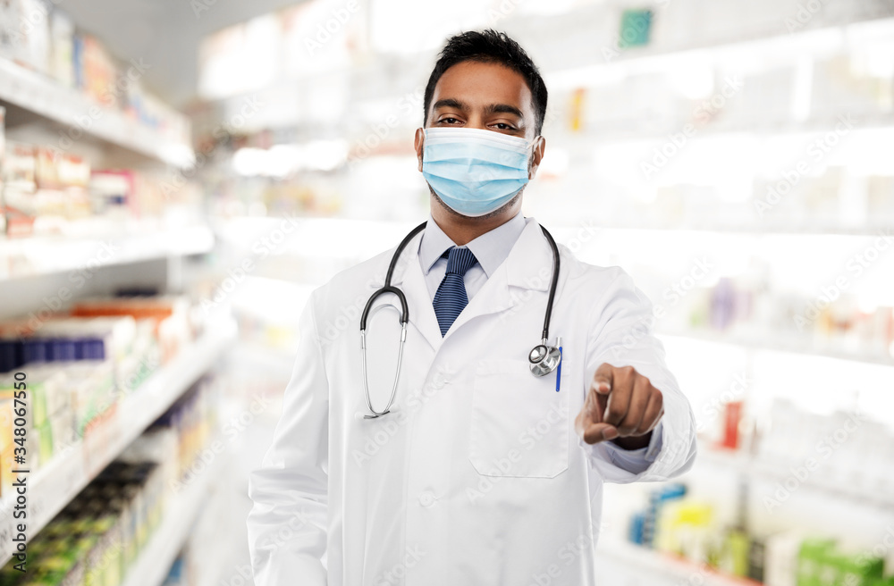 medicine, pharmacy and healthcare concept - indian male doctor or pharmacist wearing face protective medical mask with stethoscope pointing finger to you over drugstore background medicine, pharmacy and healthcare concept - indian male doctor or pharmacist wearing face protective medical mask with stethoscope pointing finger to you over drugstore background