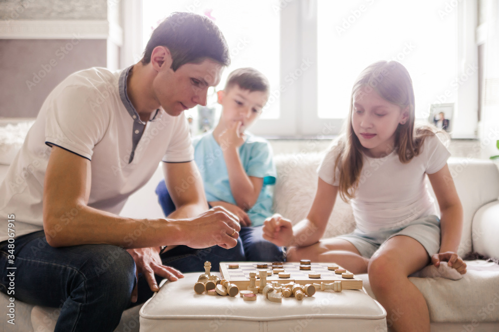 Dad, daughter and son play checkers at home together.