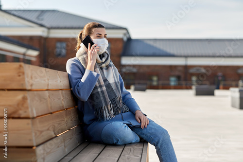 health, safety and pandemic concept - young woman wearing protective medical mask and calling on smartphone on city street