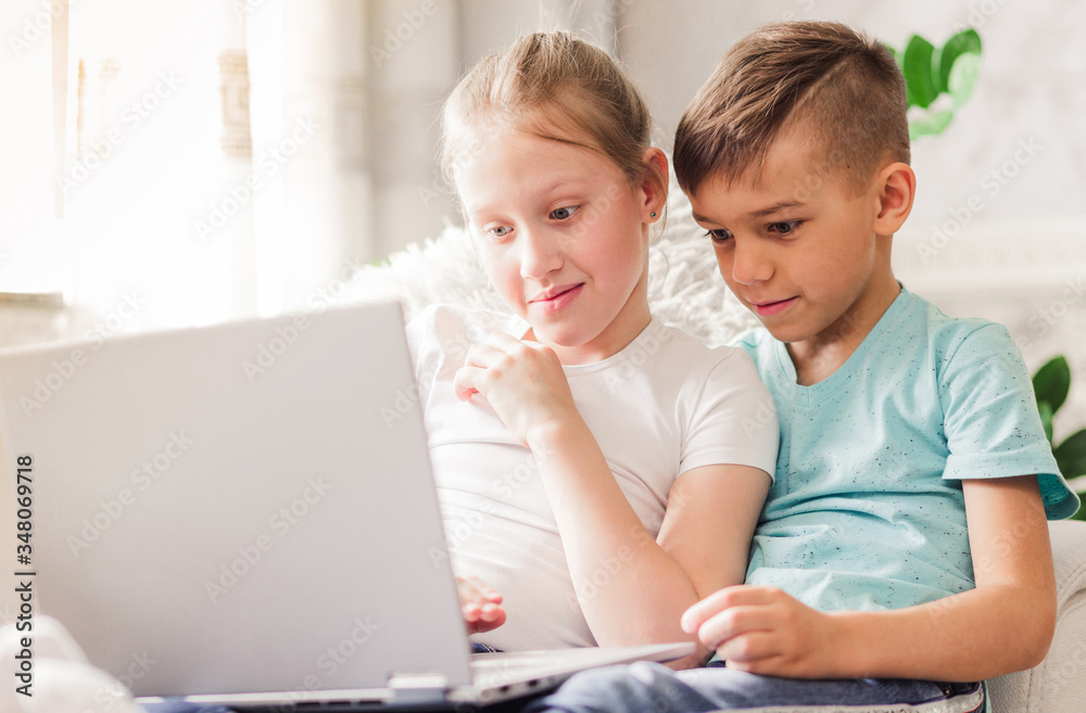 Happy brother and sister sitting on sofa at home in the living room and using laptop together. Happy brother and sister sitting on sofa at home in the living room and using laptop together.