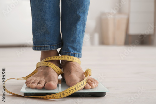 Εκτύπωση καμβά Young man with measuring tape standing on scales at home