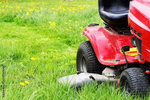 Gardener driving a riding lawn mower in a garden . Cutting grass