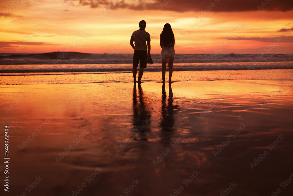 Sunset Couple. Silhouettes Of Young Man And Woman Staying Together At Beach. Vacation Or Honeymoon Concept. Walk Near Ocean At Sunrise.