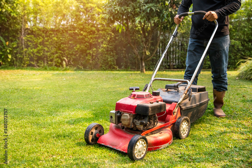 A worker cutting grass in green yard at sunset. Man with electric lawnmower, lawn mowing. Gardener trimming a garden A worker cutting grass in green yard at sunset. Man with electric lawnmower, lawn mowing. Gardener trimming a garden