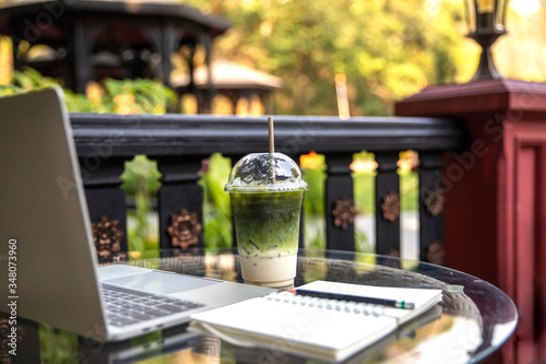 Matcha Milk , Milk Green tea latte with laptop and note book on glass table outdoors on nature background