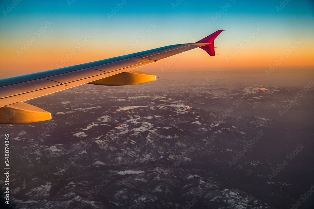 Fototapeta premium Airplane wings in sunset over mountains