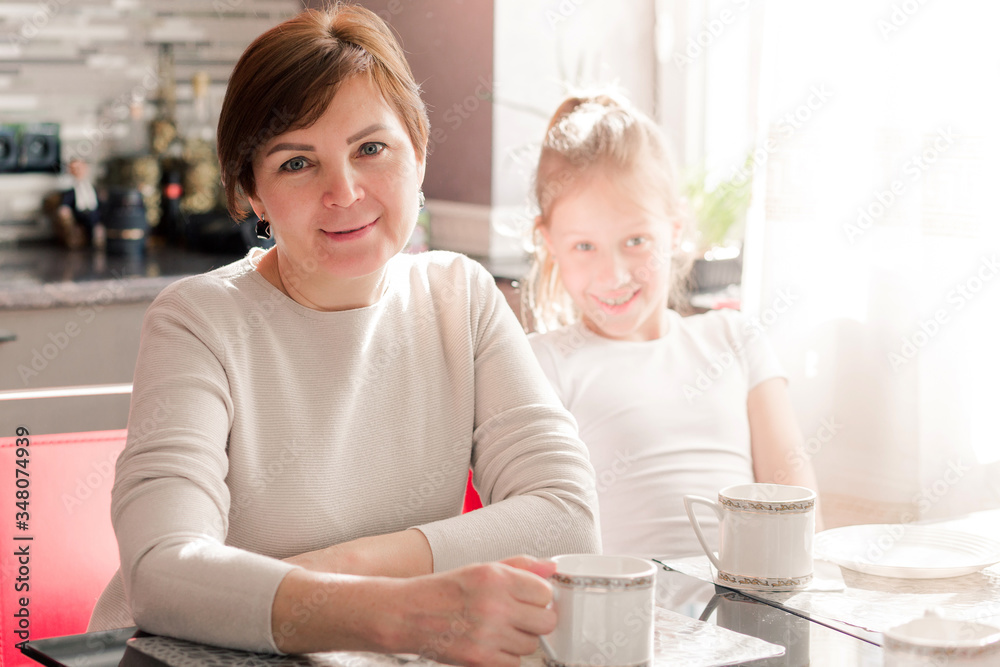 Middle aged woman is r drinking coffee or tea at cozy home kitchen. Senior person has rest from housework and cooking. Happy housewife is smiling and looking at camera Middle aged woman is r drinking coffee or tea at cozy home kitchen. Senior person has rest from housework and cooking. Happy housewife is smiling and looking at camera