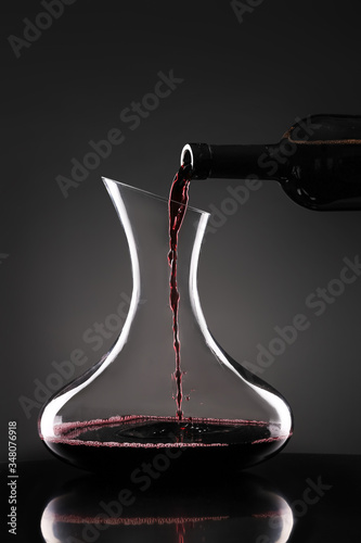 Obraz na plátně Pouring of tasty wine from bottle into glass on dark background