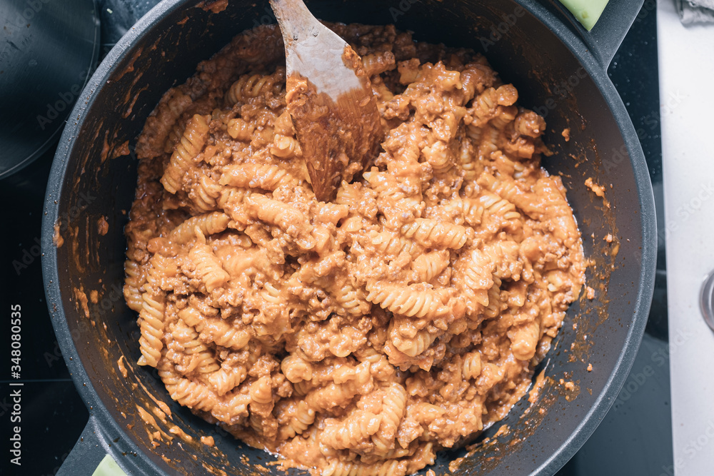 Cooking bolognese pasta fusilli on a black pan with a wooden spoon in a domestic kitchen Cooking bolognese pasta fusilli on a black pan with a wooden spoon in a domestic kitchen