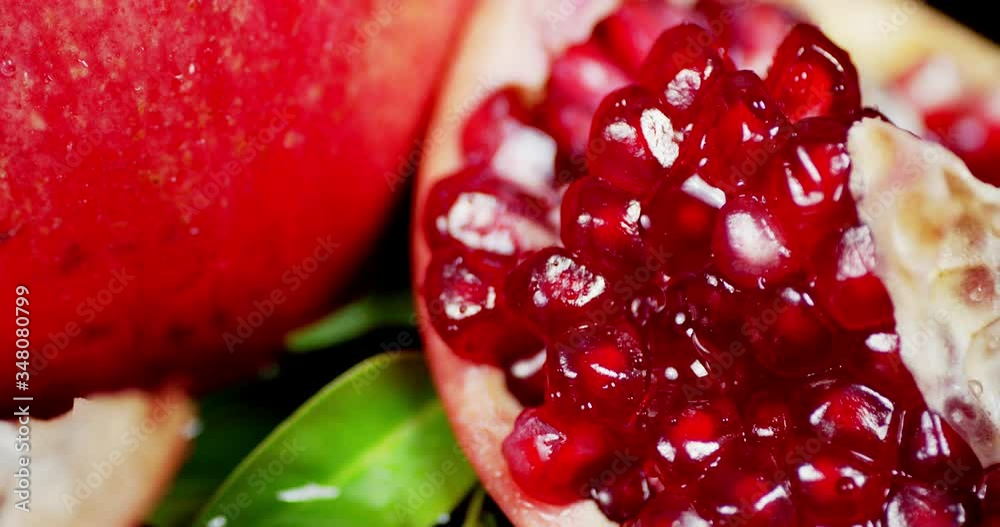 A piece of a pomegranate with leaves falling drops of water.