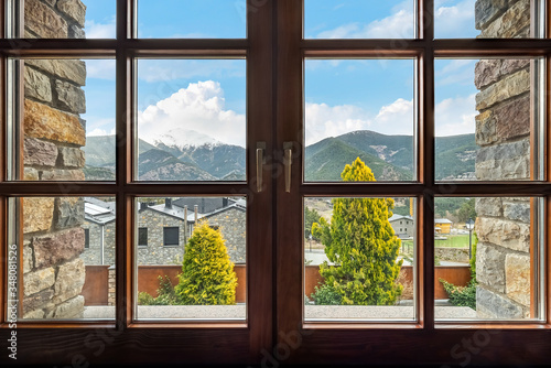Window with a view to the ridge of mountains  snow-capped peak  clouds  sky  trees and houses in Andorra.