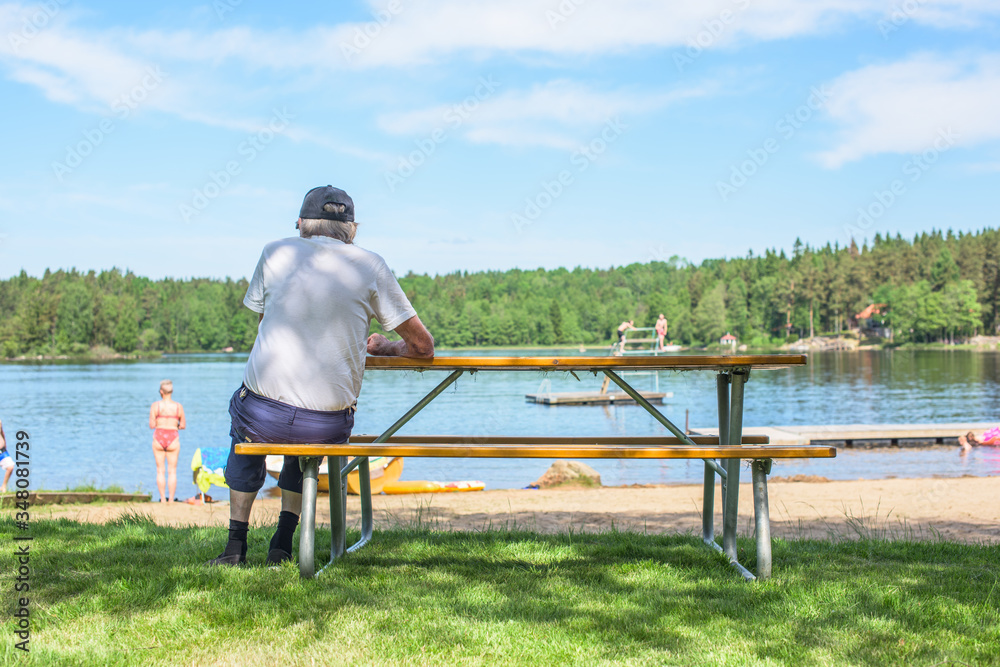 Old man with a cap sitting on a bench watching a lake beach Old man with a cap sitting on a bench watching a lake beach