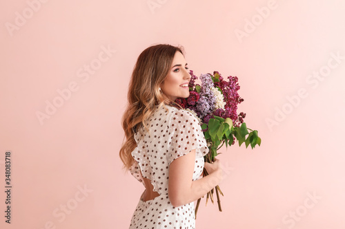 Beautiful young woman with lilac flowers on color background