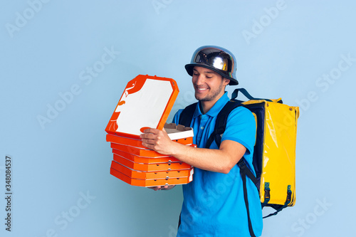 Proposing pizza. Emotions of caucasian deliveryman isolated on blue background. Contacless delivery service during quarantine. Man delivers food during isolation. Safety. Hurrying up. Looks fun. photo